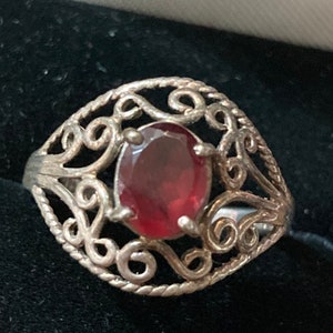 May include: A silver ring with a red gemstone set in a filigree design.