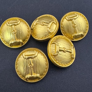 May include: Five gold-toned buttons featuring a raised design of a horse bit. The buttons have a textured surface and a slightly rounded shape.