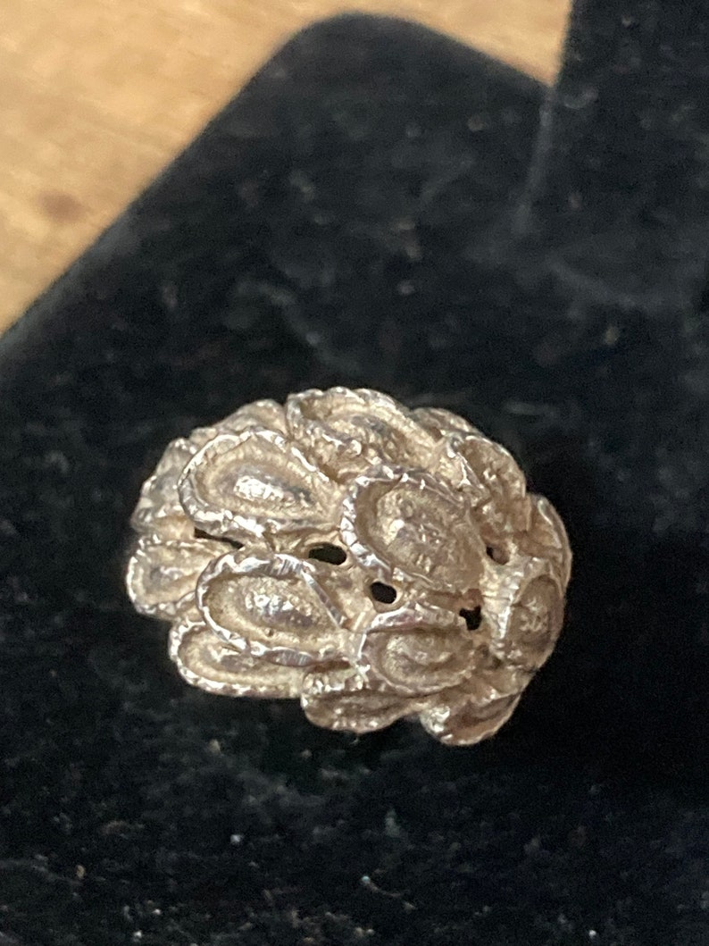 May include: A silver ring with a textured, organic design resembling a cluster of leaves or petals.