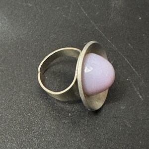 May include: A silver ring with a large, round, light purple glass stone set in a bezel setting.