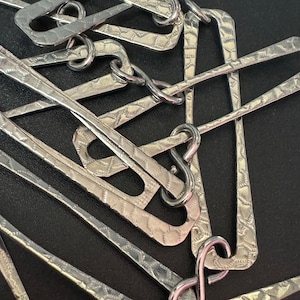 Könnte beinhalten: Nahaufnahme einer silbernen Metallkette aus ineinandergreifenden Gliedern. Jedes Glied ist mit einem sich wiederholenden Muster strukturiert. Die Kette liegt auf einer schwarzen Oberfläche.