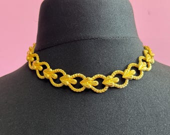 May include: A gold-tone necklace with a chain made of linked heart-shaped charms. The necklace is displayed on a black mannequin.