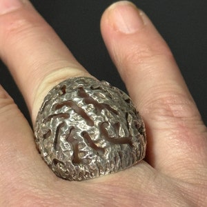 May include: A silver ring with a textured, organic design. The ring is worn on a finger.