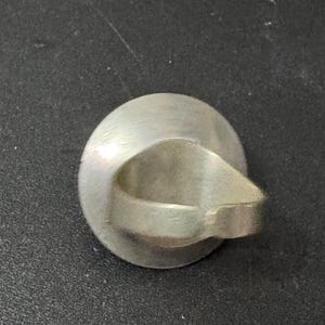 May include: A silver ring with a smooth, oval-shaped band. The ring is designed with a unique, open-ended band that creates a circular opening in the centre.
