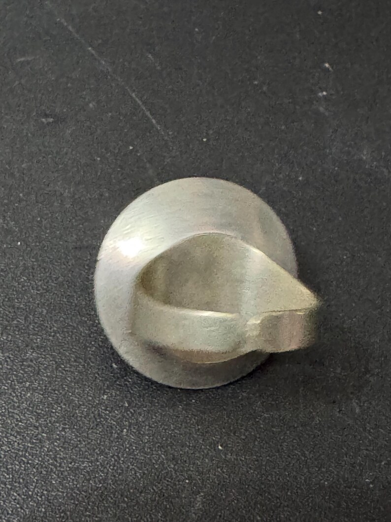 May include: A silver ring with a smooth, oval-shaped band. The ring is designed with a unique, open-ended band that creates a circular opening in the centre.