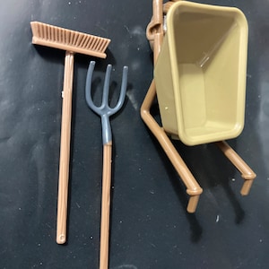 以下が含まれることがあります： 灰色のプラスチック製のハンドルと灰色のプラスチック製の熊手とフォークが付いた、茶色のプラスチック製の玩具の車輪付き手押し車です。