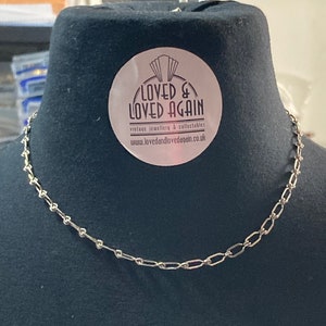 May include: A silver chain necklace on a black mannequin bust. The necklace is made of small, linked oval shapes. A sticker on the bust reads "Loved & Loved Again" vintage jewellery & collectables www.lovedandlovedagain.co.uk