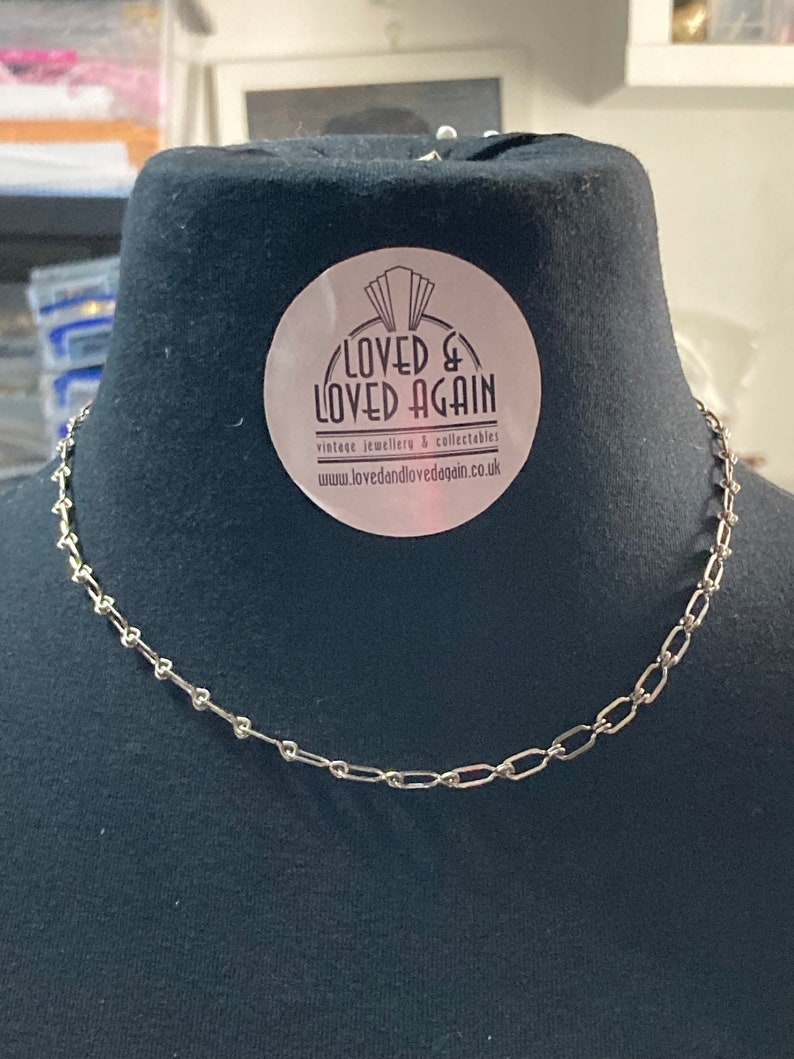May include: A silver chain necklace on a black mannequin bust. The necklace is made of small, linked oval shapes. A sticker on the bust reads "Loved & Loved Again" vintage jewellery & collectables www.lovedandlovedagain.co.uk