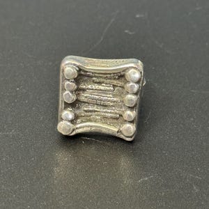 May include: A silver ring with a textured design and a row of small circles around the edge.