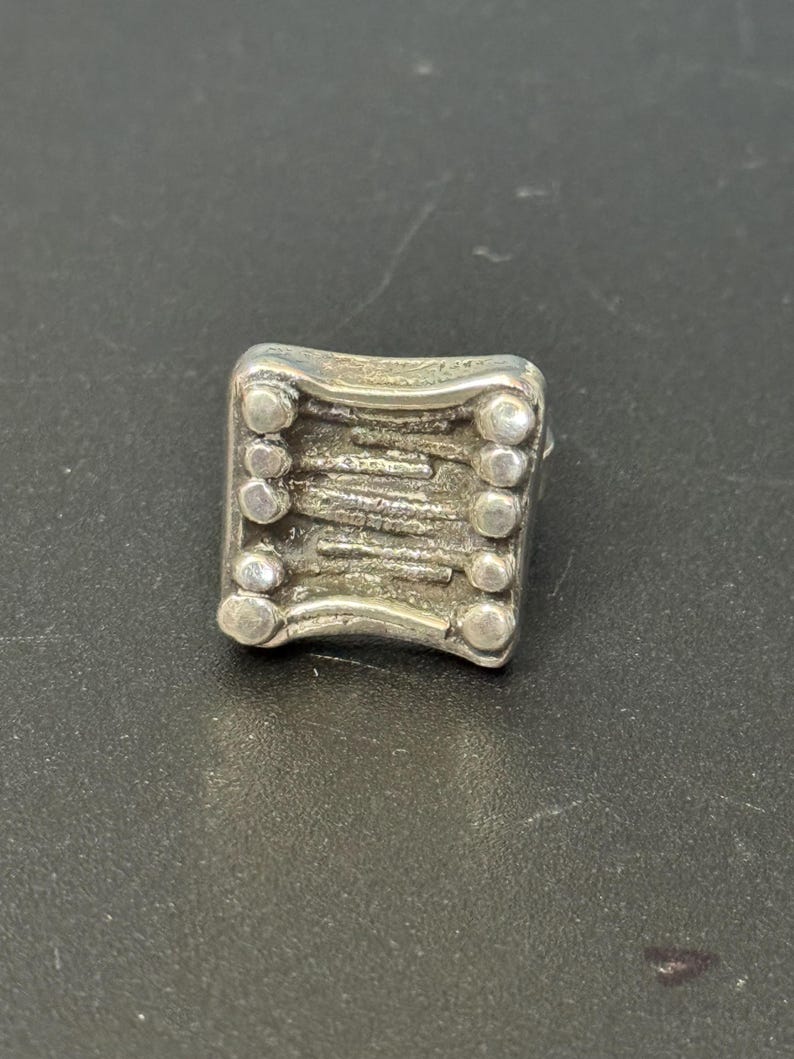 May include: A silver ring with a textured design and a row of small circles around the edge.