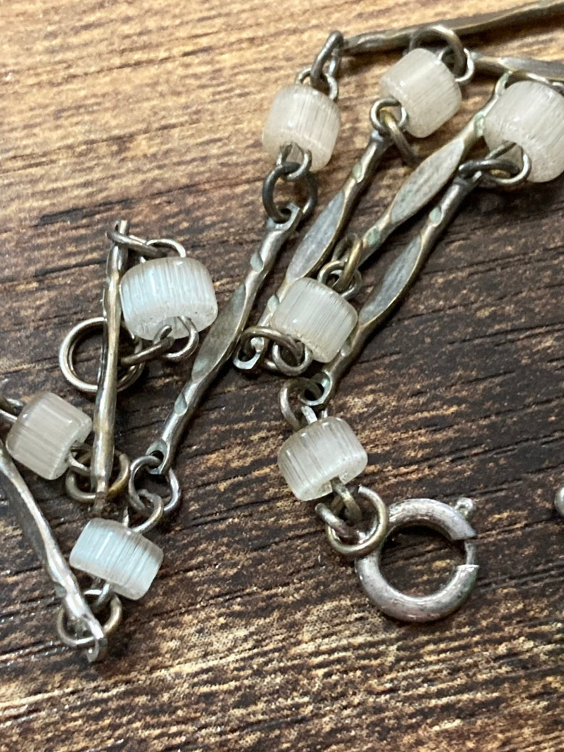 Pu&ograve; includere: Un braccialetto a catena d'argento con perline di vetro trasparenti. La catena &egrave; composta da pi&ugrave; fili di metallo intrecciato.