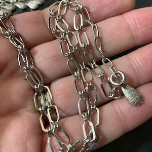 May include: Silver chain necklace with a small, teardrop-shaped pendant.