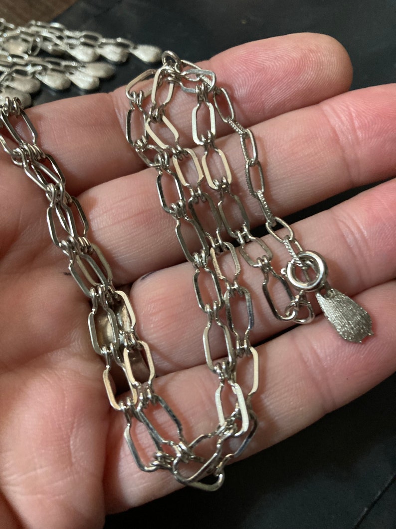 May include: Silver chain necklace with a small, teardrop-shaped pendant.