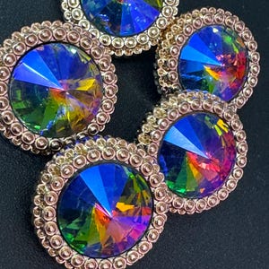 May include: Five iridescent rainbow-coloured crystal rhinestones with gold-toned metal settings. The rhinestones are arranged in a circular pattern.