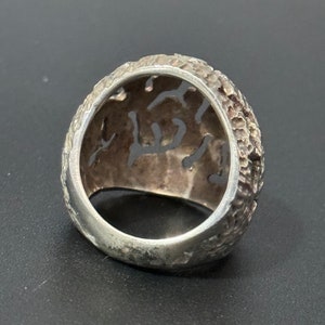 May include: A silver ring with a textured, intricate design. The ring is made of a single piece of metal and has a wide band.