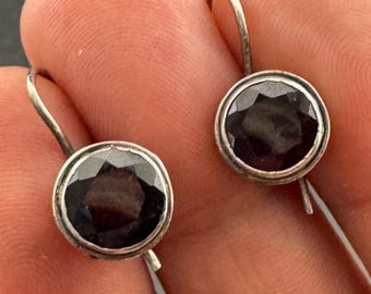 May include: A pair of silver earrings with dark gray gemstone accents. The earrings have a simple, elegant design.