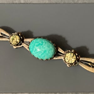 May include: A silver brooch featuring a turquoise stone and two clear rhinestones.