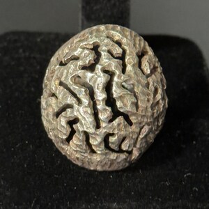 May include: A silver ring with a textured, abstract design. The ring is round and has a raised, intricate pattern.