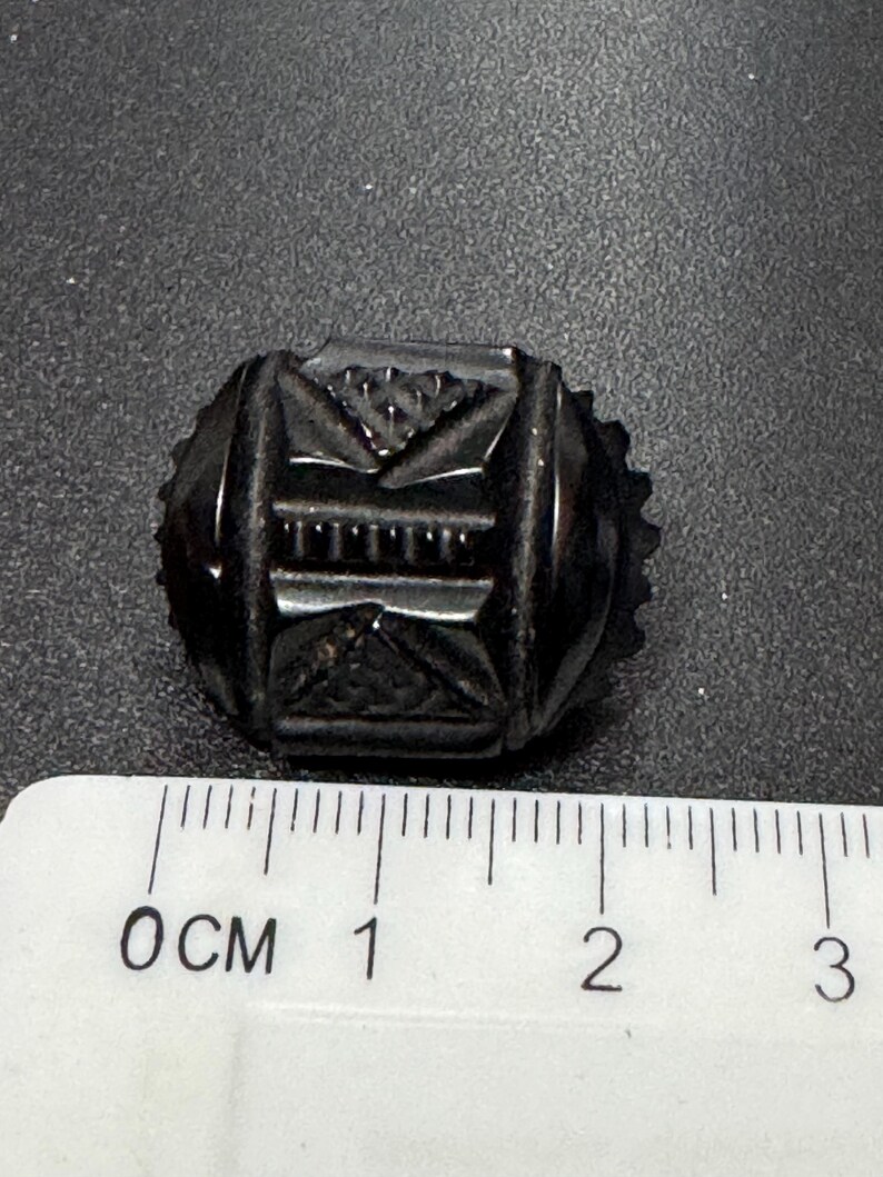 May include: A black glass button with a geometric design. The button is approximately 1 cm in diameter.