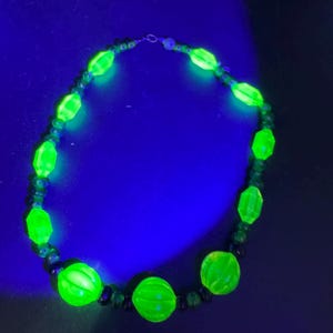 May include: A necklace featuring large, luminous green beads and smaller, dark green beads. The necklace is displayed against a dark blue backdrop, creating a vivid contrast. The beads have a distinctive, textured appearance.