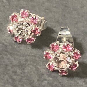 May include: A pair of silver stud earrings with a pink rhinestone cluster in the centre of each earring.