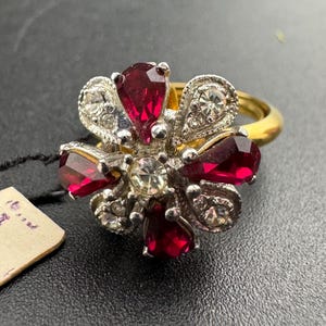 Könnte beinhalten: Ein goldener Ring mit einem roten und klaren Strass-Blumenmuster.