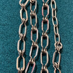 May include: Three silver chains with a linked oval design. The chains are laid out side by side on a blue surface.