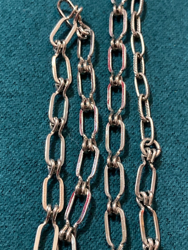 May include: Three silver chains with a linked oval design. The chains are laid out side by side on a blue surface.