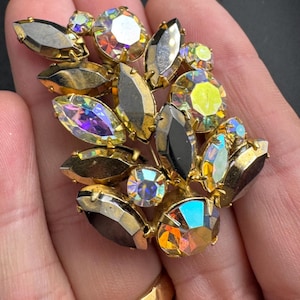 May include: Vintage gold-toned brooch with a cluster of iridescent and black crystal stones. The brooch features a floral design with various shapes and sizes of crystals, creating a sparkling effect. A classic accessory.