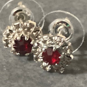 Puede incluir: Un par de pendientes de bot&oacute;n de plata con piedras preciosas rojas rodeadas de piedras preciosas transparentes m&aacute;s peque&ntilde;as.