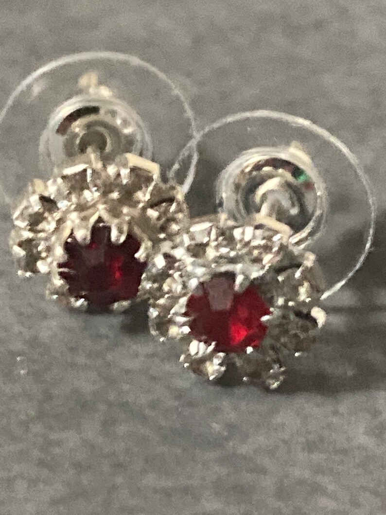 Puede incluir: Un par de pendientes de bot&oacute;n de plata con piedras preciosas rojas rodeadas de piedras preciosas transparentes m&aacute;s peque&ntilde;as.