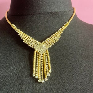 May include: A gold necklace with a V-shaped design and a dangling fringe of rhinestones.