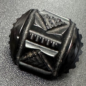 May include: A black, intricately carved, geometric button with a raised design.