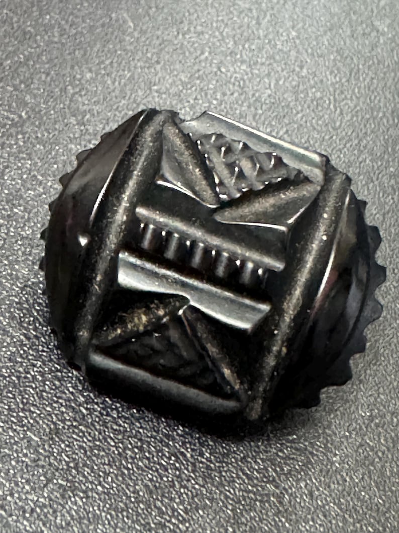May include: A black, intricately carved, geometric button with a raised design.