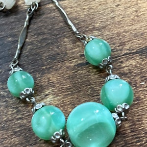 Pu&ograve; includere: Una collana a catena d'argento con perline di vetro verde. Le perline hanno un motivo a spirale e sono collegate da anelli d'argento.