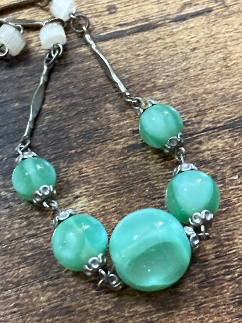 Pu&ograve; includere: Una collana a catena d'argento con perline di vetro verde. Le perline hanno un motivo a spirale e sono collegate da anelli d'argento.