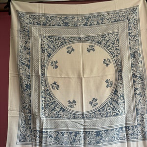 May include: A white tablecloth with a blue and white floral pattern. The pattern features a repeating design of stylised flowers and houses.