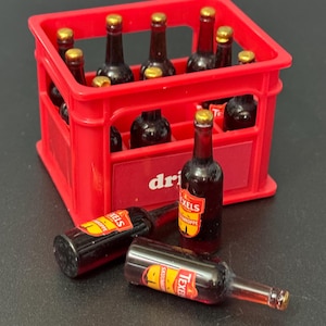 May include: A red plastic crate filled with miniature glass bottles of beer. Two bottles are lying outside the crate. One bottle has a label that reads "Texel Skuimkoppe".
