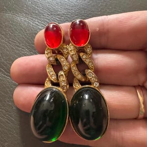 May include: A pair of gold-tone drop earrings featuring a red oval cabochon at the top, a central chain link section encrusted with clear rhinestones, and a large, smooth, dark green oval cabochon at the base of each earring.