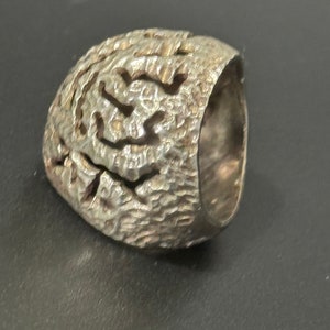 May include: A silver ring with a textured, organic design. The ring is made of a single piece of metal and has a smooth, rounded band.