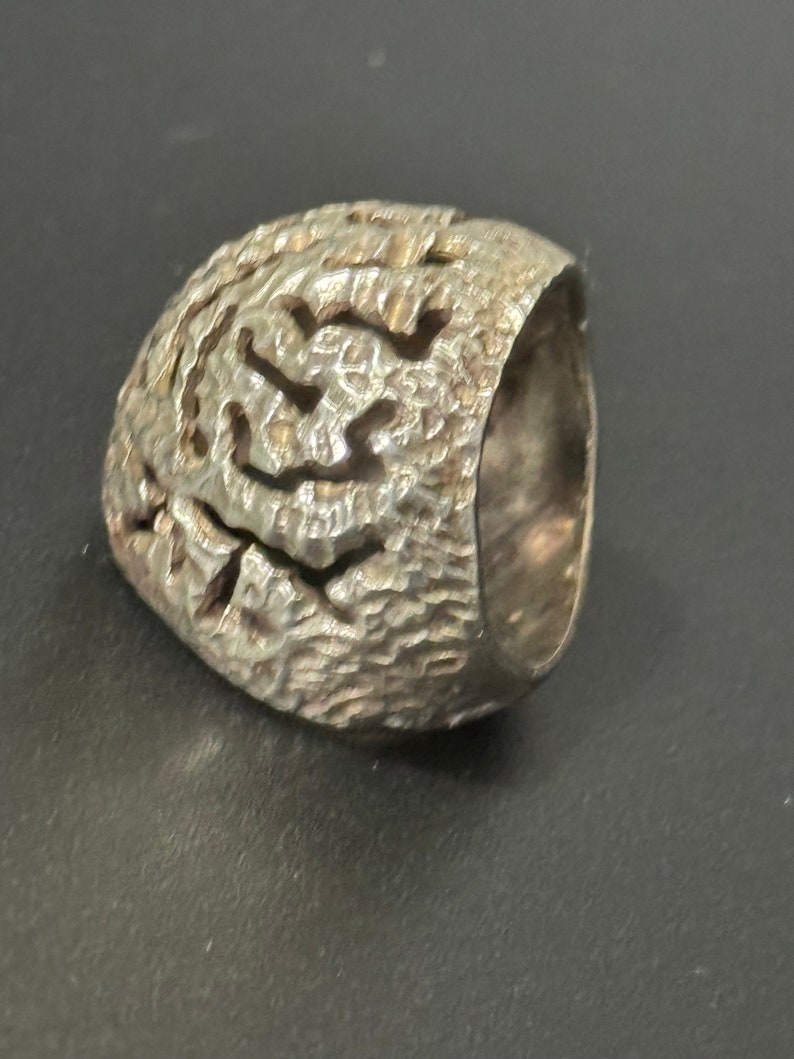 May include: A silver ring with a textured, organic design. The ring is made of a single piece of metal and has a smooth, rounded band.