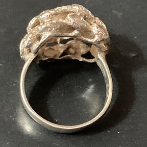 May include: A silver ring with a textured, organic design. The ring is made of a single piece of metal and has a smooth, polished finish.