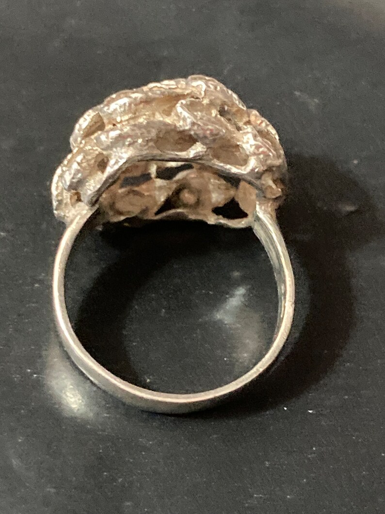 May include: A silver ring with a textured, organic design. The ring is made of a single piece of metal and has a smooth, polished finish.