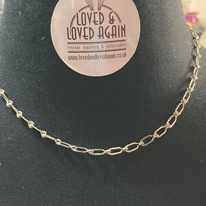 May include: A silver chain necklace with a delicate, linked design. The chain is made of small, oval-shaped links.