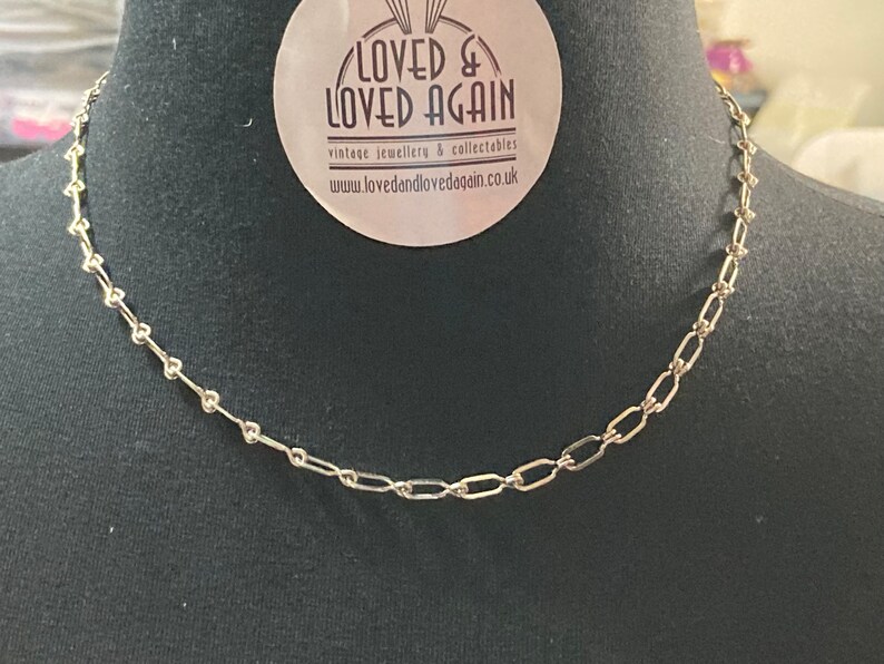 May include: A silver chain necklace with a delicate, linked design. The chain is made of small, oval-shaped links.