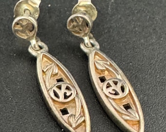 May include: A pair of silver-toned dangle earrings. Each earring features an elongated oval shape with a cutout design and a central peace symbol. The earrings have a post backing for pierced ears.