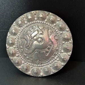 May include: A silver circular brooch with a decorative design of a stylised bird or animal with a floral border.