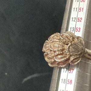 May include: A silver ring with a detailed floral design. The ring is being measured with a ring sizer, showing a size of 17.5.