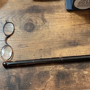 May include: A black folding magnifying glass with a brown tortoiseshell handle. The magnifying glass is closed and the handle is extended.