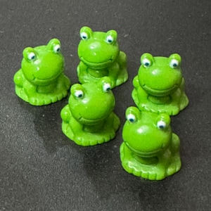 May include: Five green frog figurines with white eyes. The frogs are sitting with their legs tucked under them.